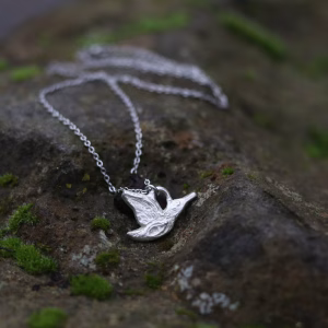 A sterling silver queenfisher necklace rests on a mossy rock
