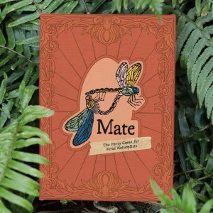 Mate: The Party Game for Feral Naturalists box in a bed of ferns. It has an ornate victorian banner and depicts two mating linocut dragonflies.